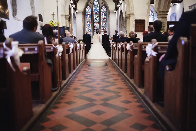 Wide shot from behind of bride and groom as they stand at the altar for their weddingat St Mary's church in Kent