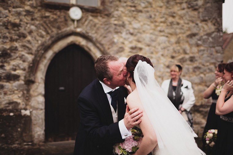 Father of the groom kissing the bide on the cheek after her wedding ceremony at St Mary's Church in Kent
