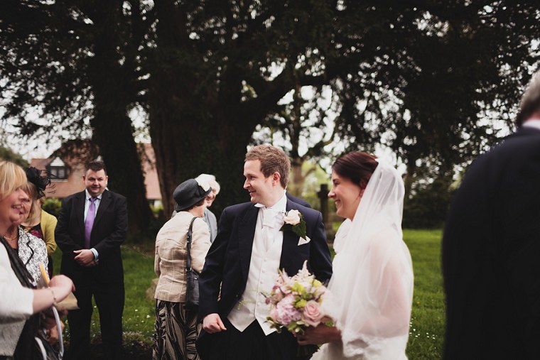 Bride and Groom laughing together after their wedding service in front of Saint Mary's church in Kent